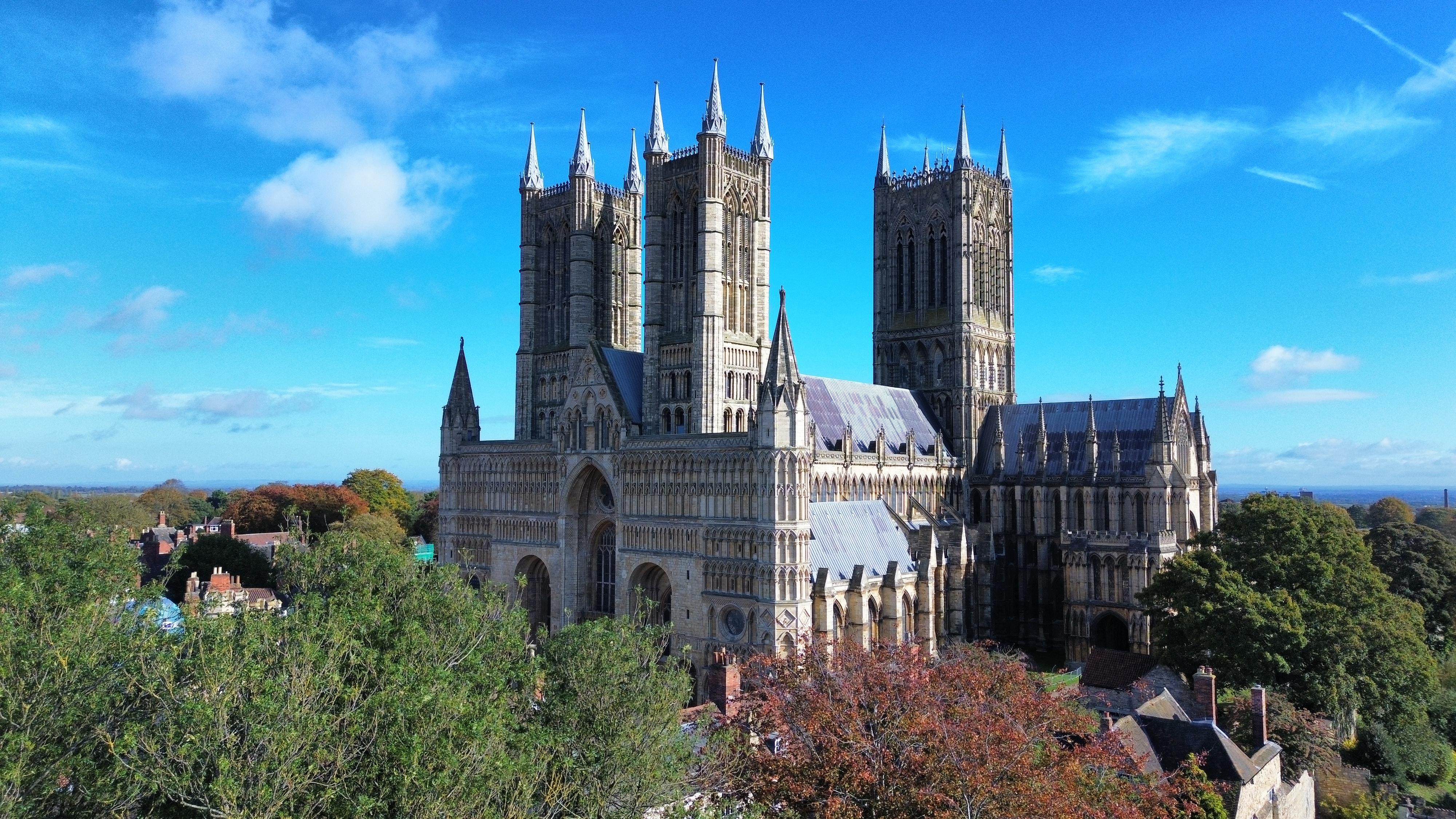 Aerial photo of Lincoln Cathedral which shows the Cathedral surrounded by trees below and sunny blues sky above.