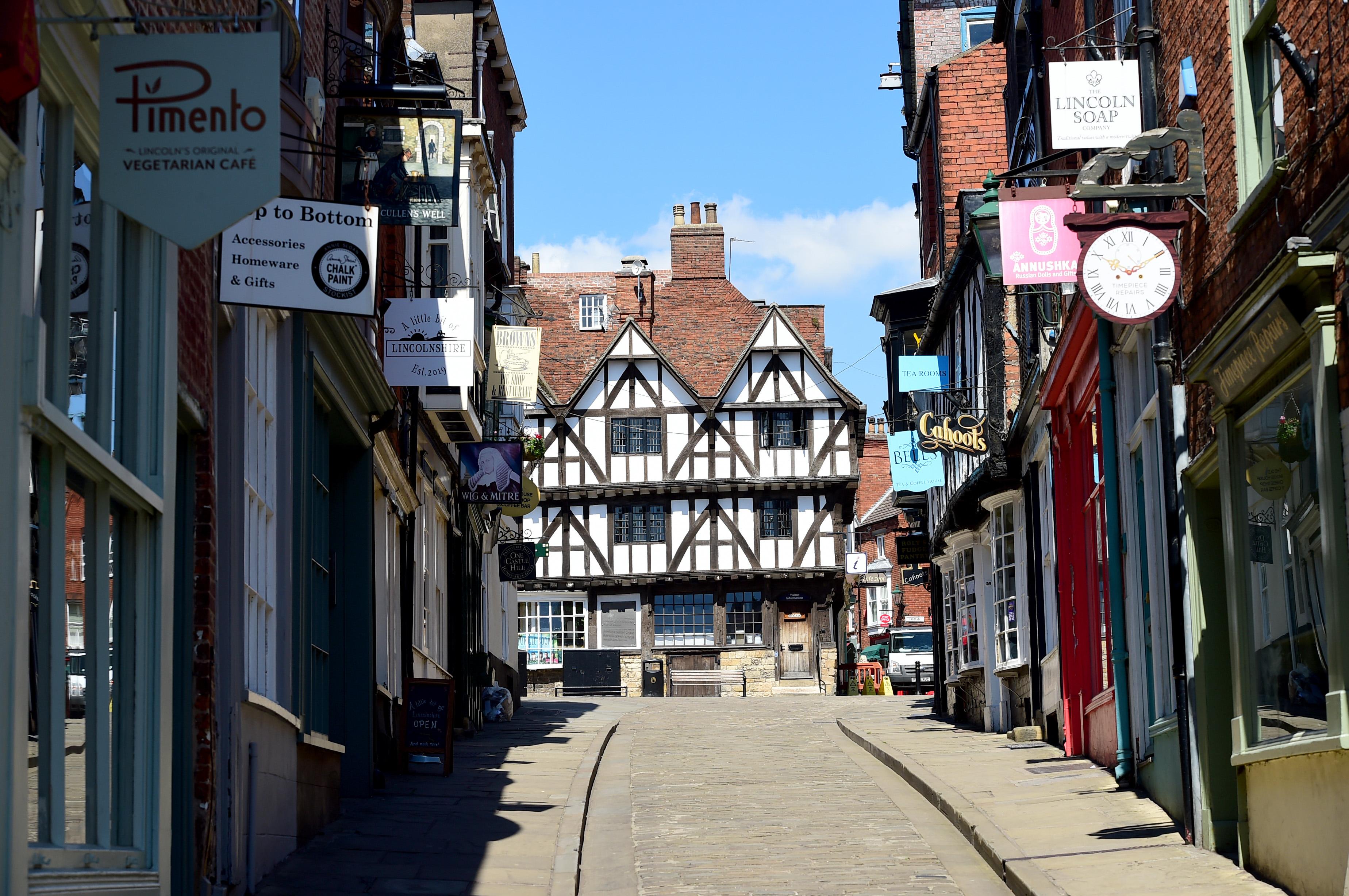 The path going up Steep Hill with shops either side of it. At the top of the hill there is a beautiful black and white building, Lincoln Visitor Information Centre.