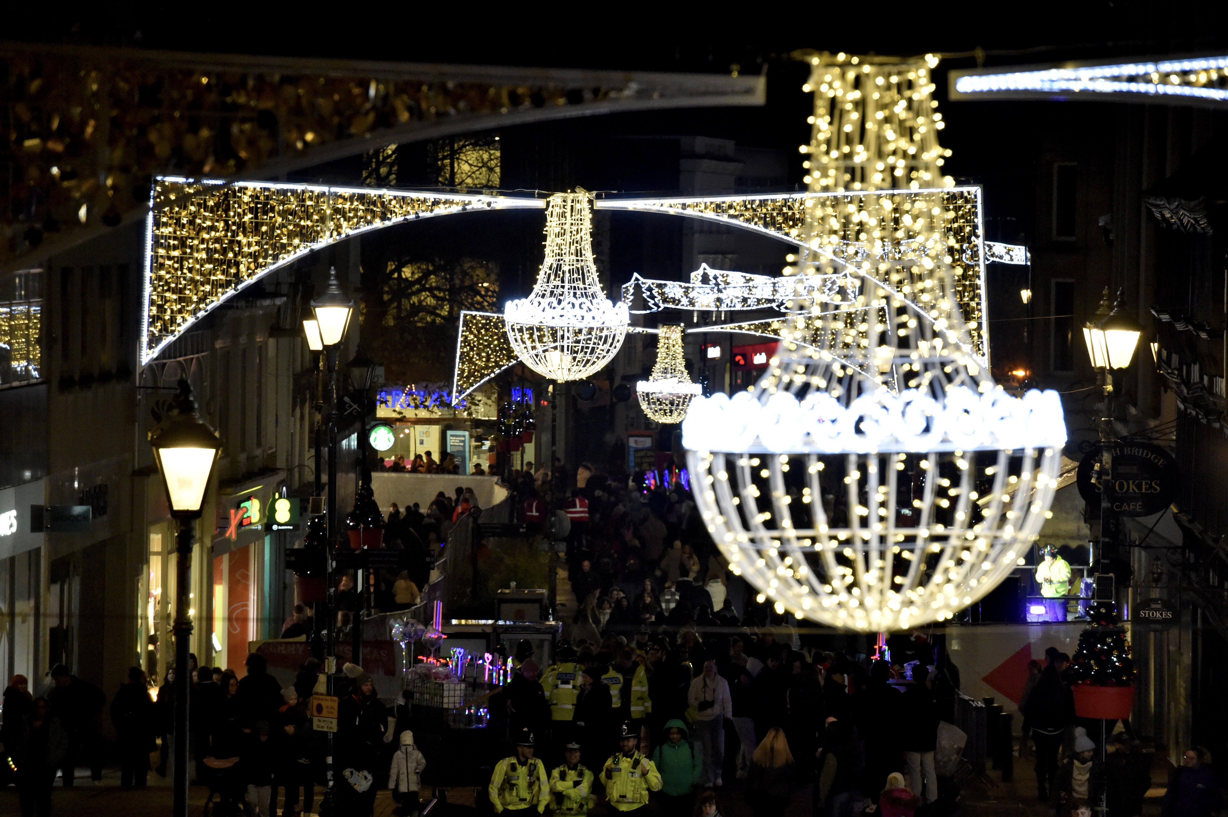 Close up of golden sparkly Christmas lights above Lincoln High Street. Big crowds of people can be seen walking along the street below.