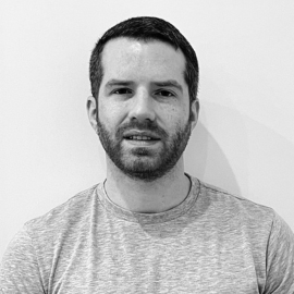 A greyscale image of Matt, he wears a grey t-shirt and is stood against a plain white wall.