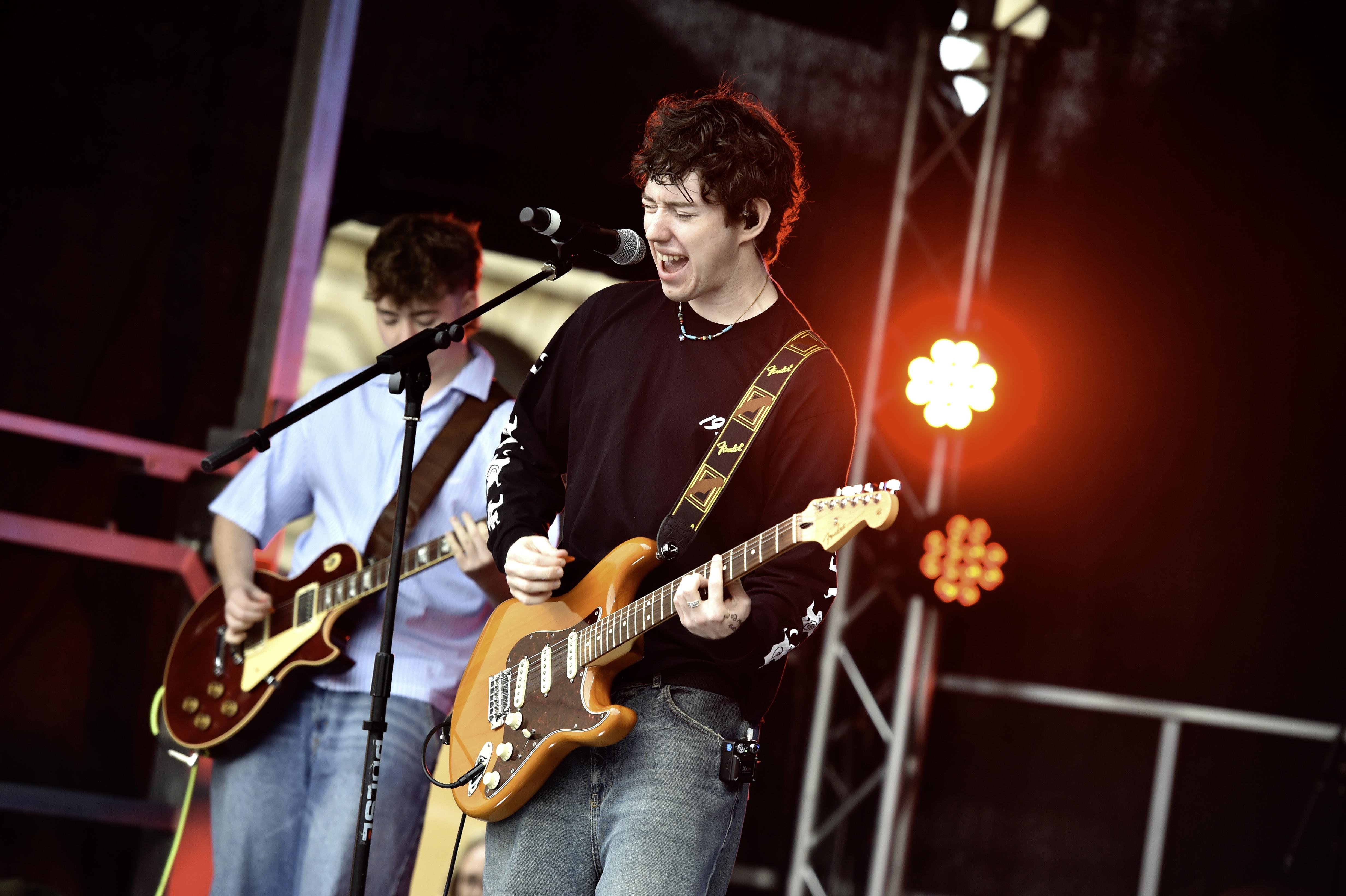 Two young males on stage, both with guitars and one singing.