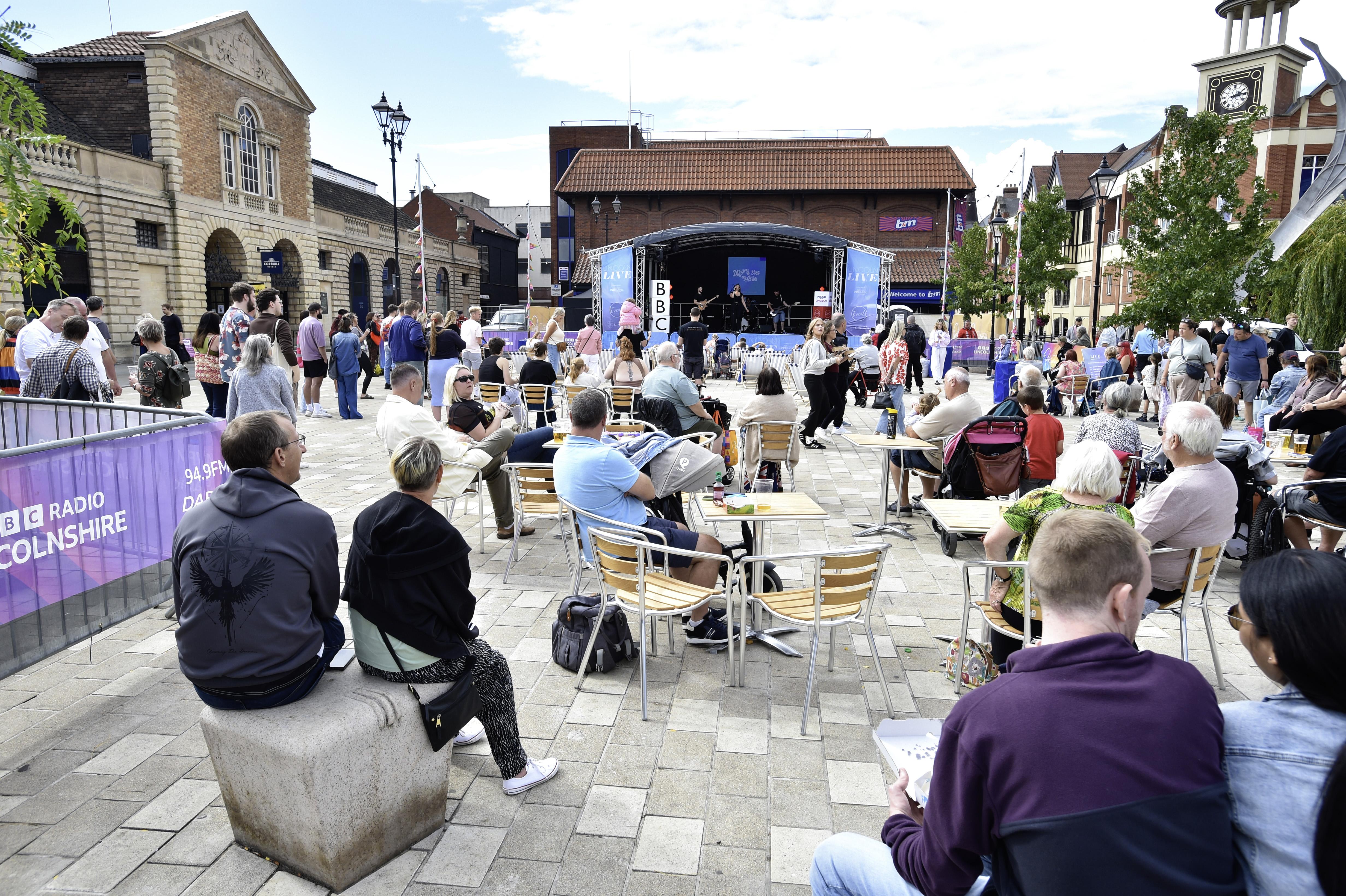 Groups of people stood and sat in front of the Lincoln Live branded stage on City Square.