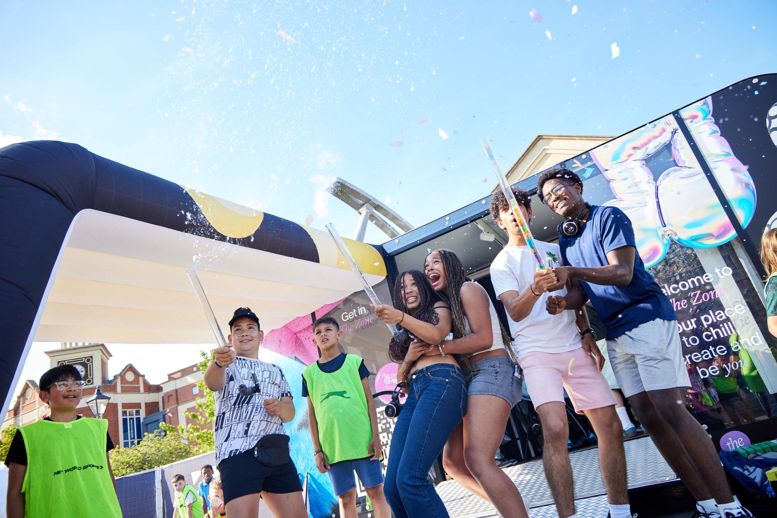 A group of young adults set off party confetti outside The Zone.