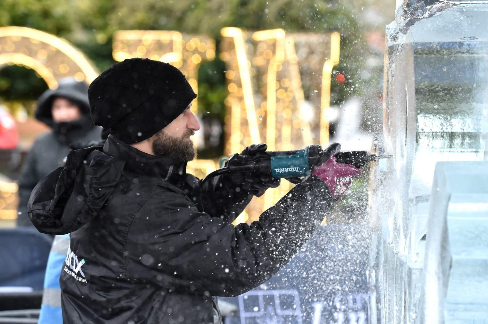 A man with a drill sculpting an ice sculpture.