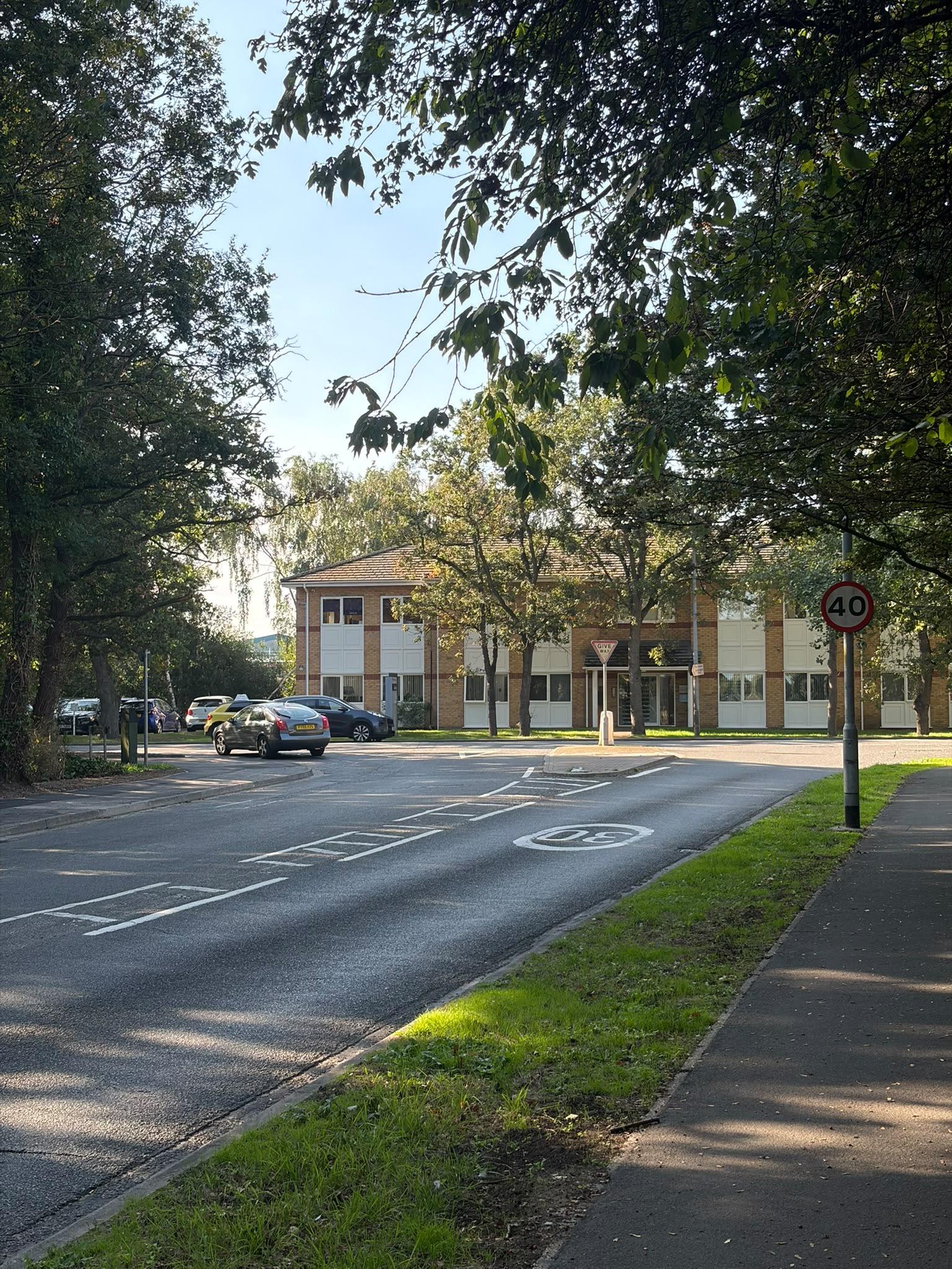 A main road junction with trees on the corner as you look at the junction.