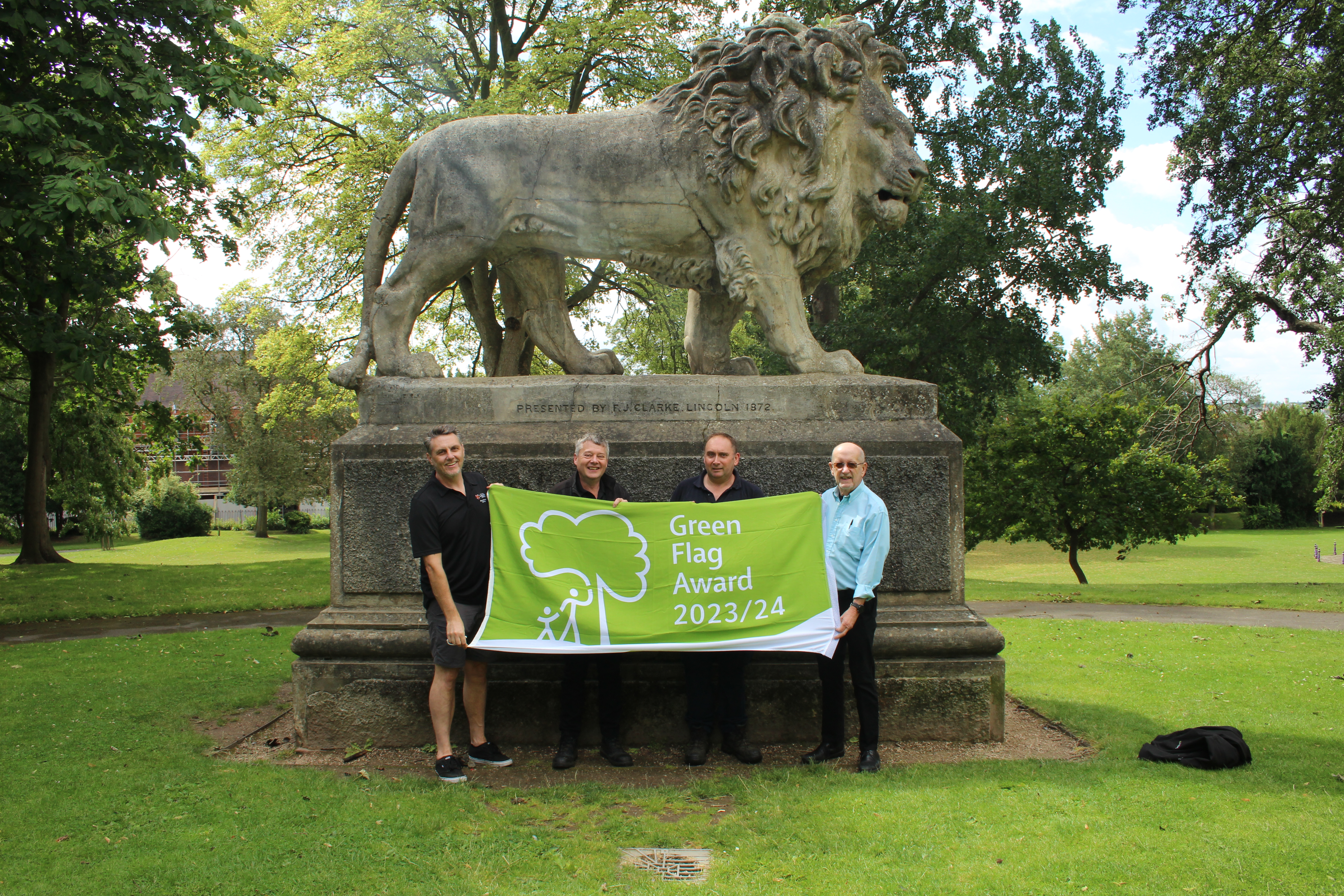 four people holding green flag outside in Arboretum park