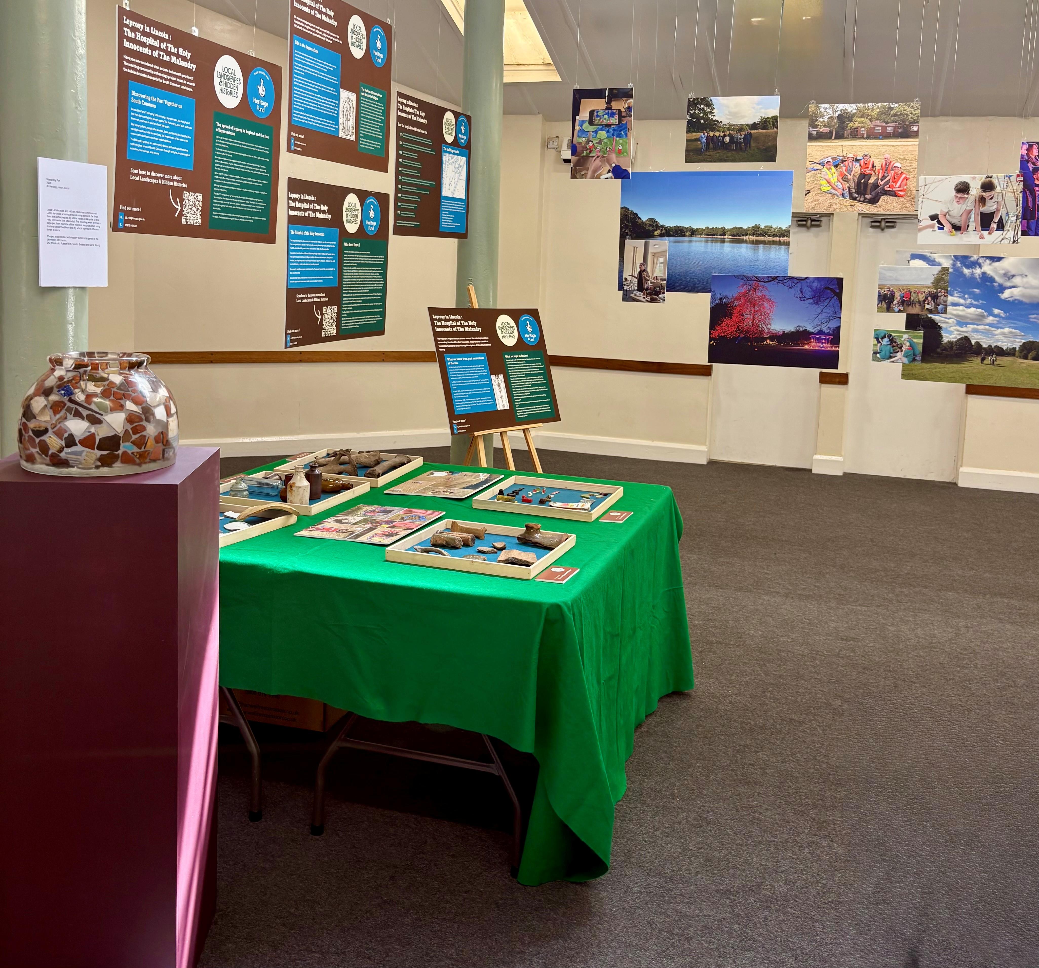 A table with a green cloth in an empty room with lots of pictures on the walls and hanging from the ceiling.