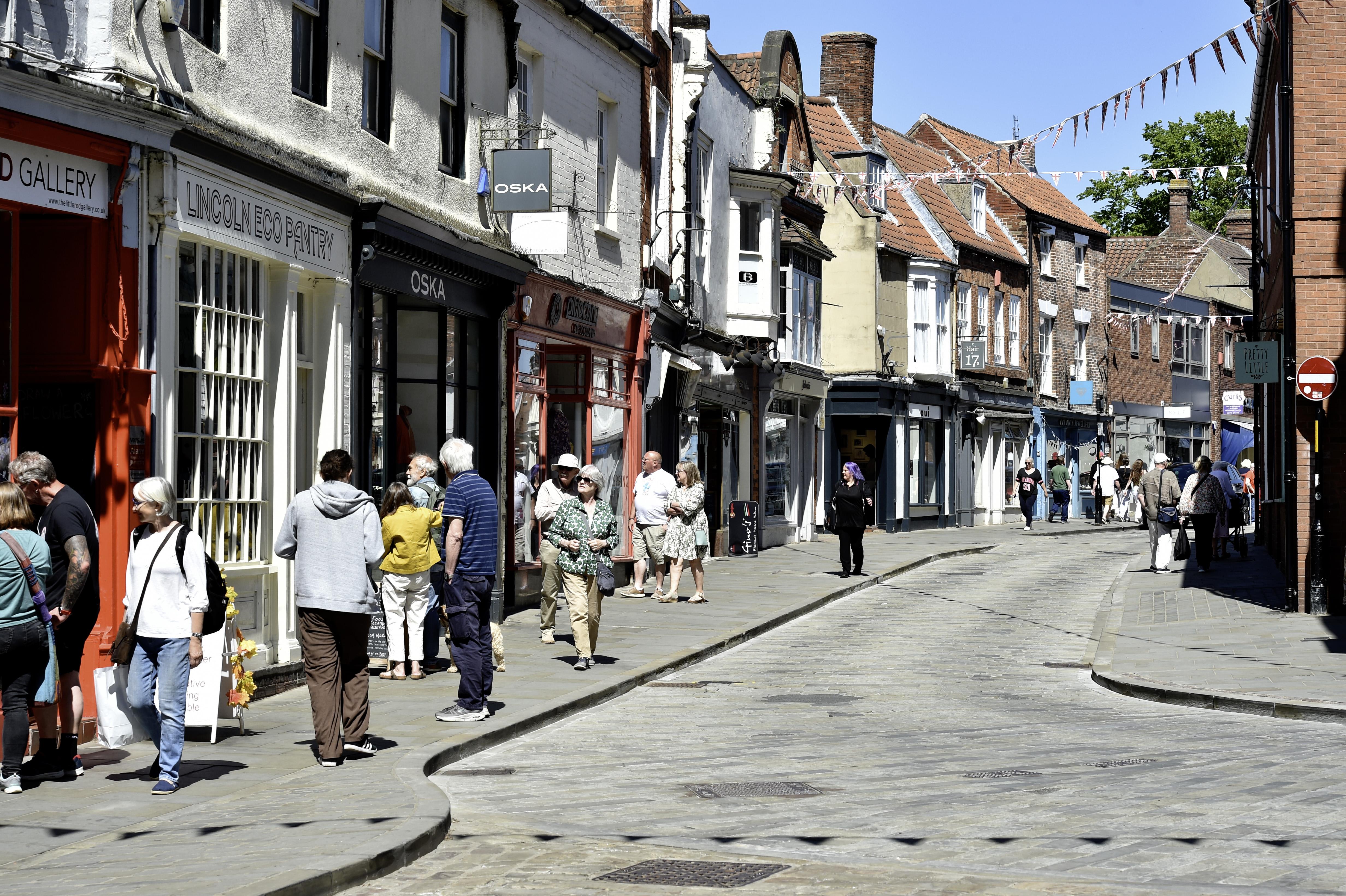 A picture of a quaint cobbled street in Lincoln's Bailgate area on a clear sunny day with many shoppers on the path.