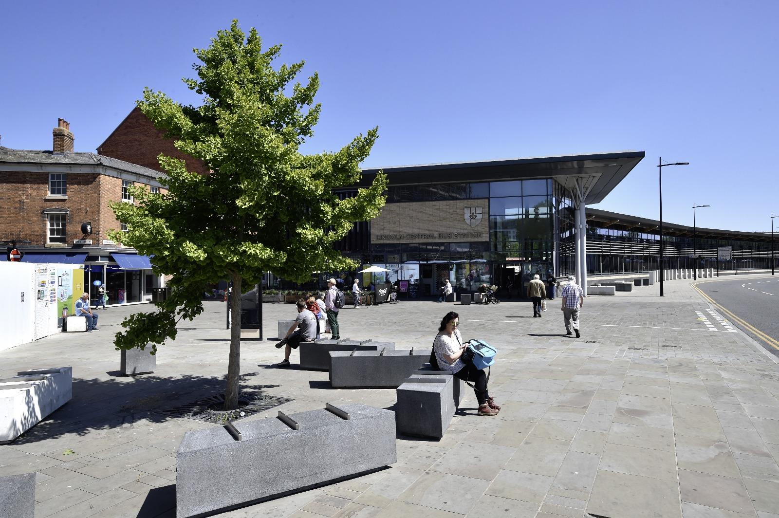 The front of the bus station with a tree in the forefront and stone blocks for people to sit on.