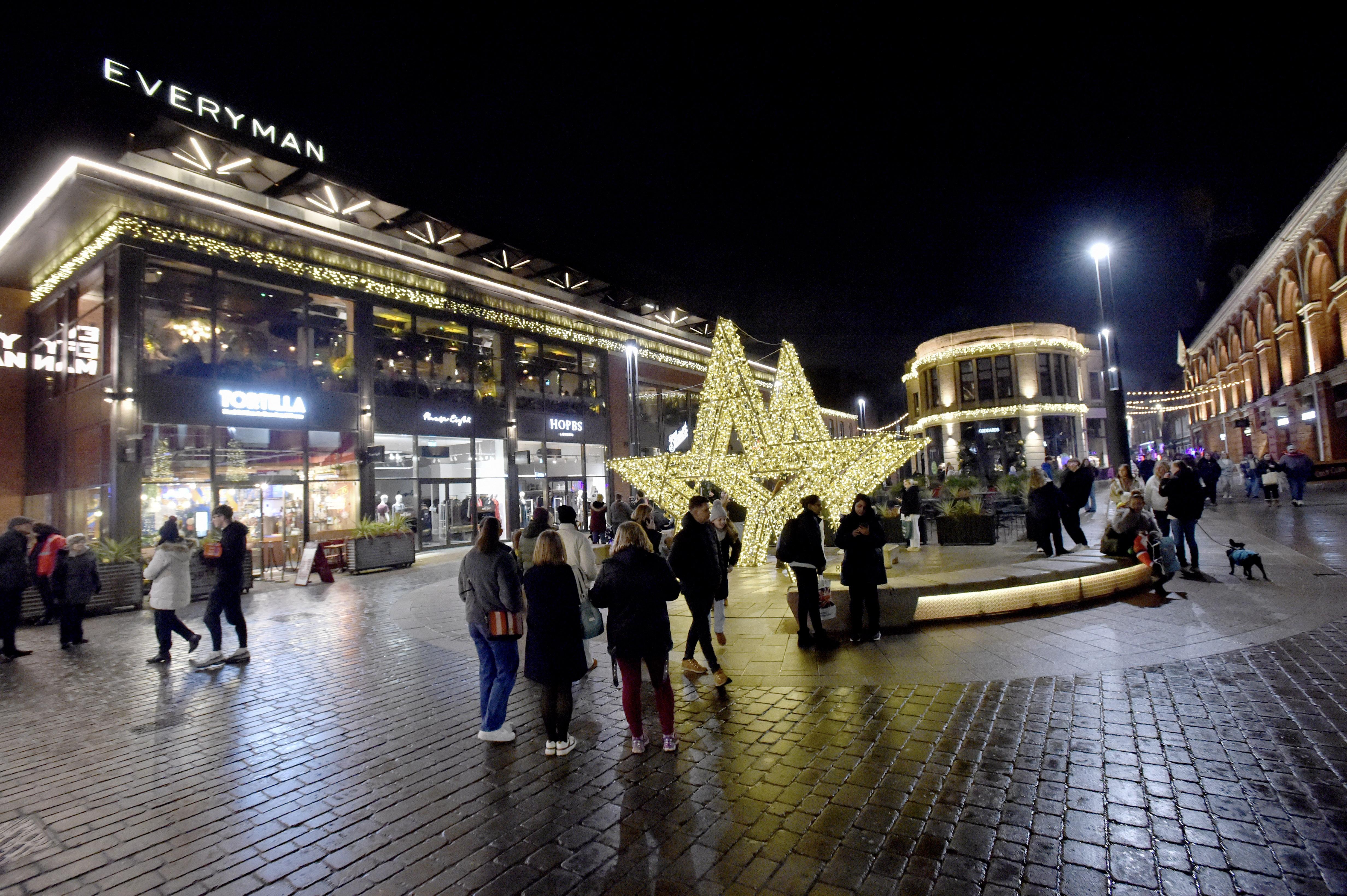Night time at Cornhill in Lincoln City Centre – there are Christmas lights in the middle of the walkway with restaurants lit up on either side and people walking around.