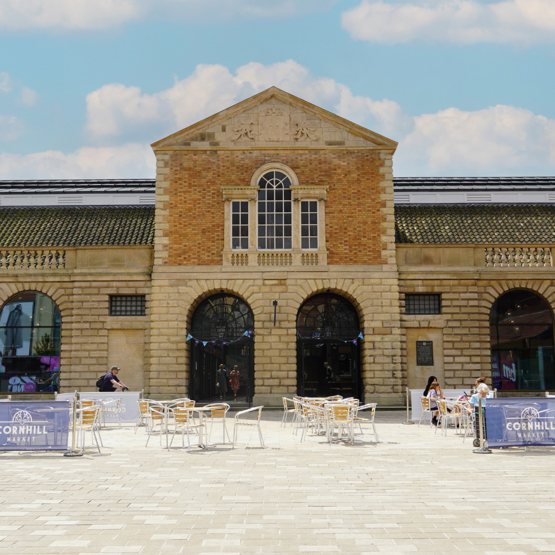 The main entrance to the Cornhill Market on a bright sunny day, with an outdoor seating area in front.