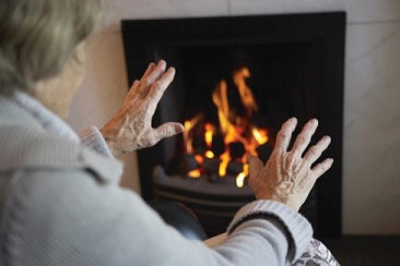 Elderly person holding their hands up to a fireplace