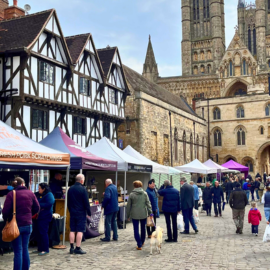 Stalls set up at the Lincoln Farmers' Market in Castle Square. People in coats with shopping bags browse the stalls.