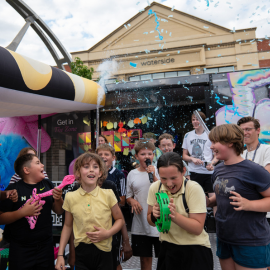 School children roughly aged 9 to 11 dancing at The Zone with inflatable instruments, confetti and tambourines, all looking very happy.