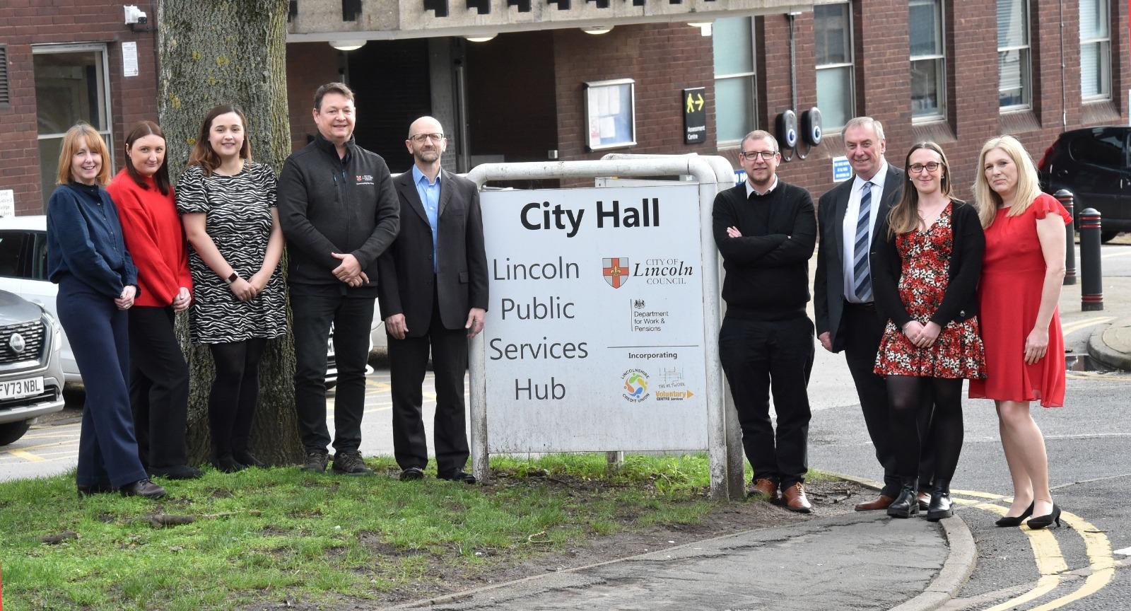 A mix of nine men and women dressed corporately stood either side of the City Hall sign outside.