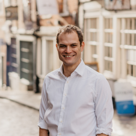 Hamish stands smiling in a white shirt, with Steep Hill out of focus in the background.