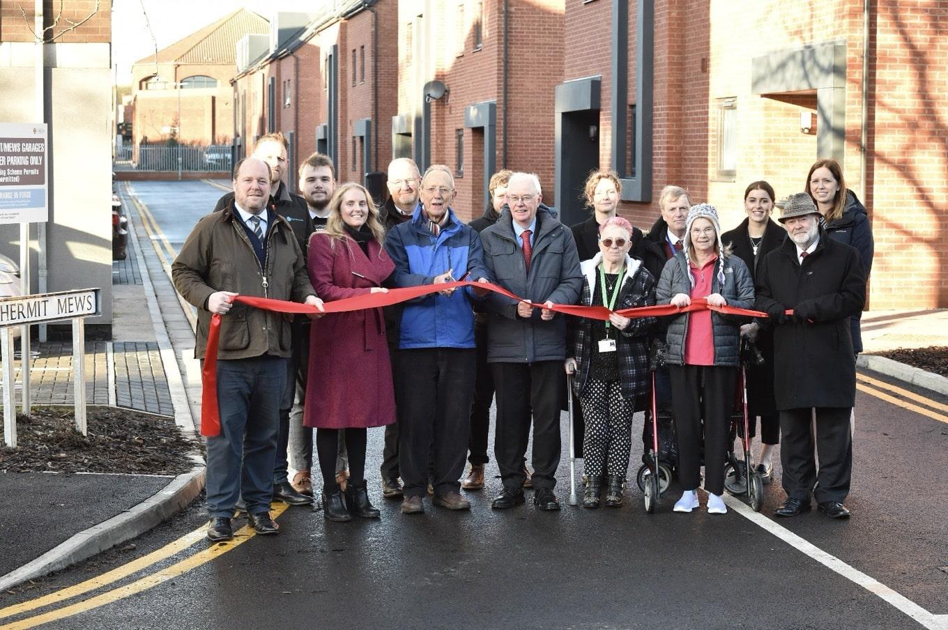 A group of people stood holding a red ribbon on a new street
