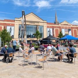 Blue skies overlook City Square, with people sat at tables and stalls in the background.