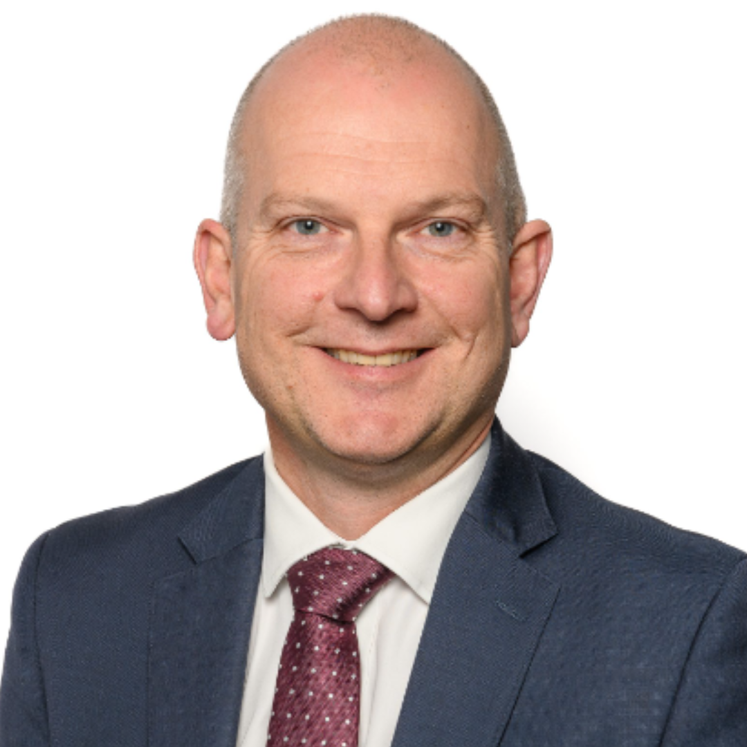 James foster smiles for a headshot against a white background, he wears a suit and tie.
