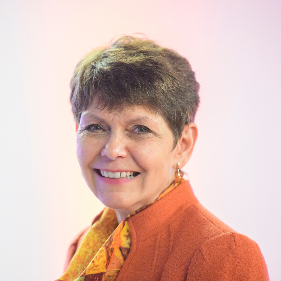 Jacqui Bunce wears a colourful orange top and smiles for the camera against a pale pastel background.