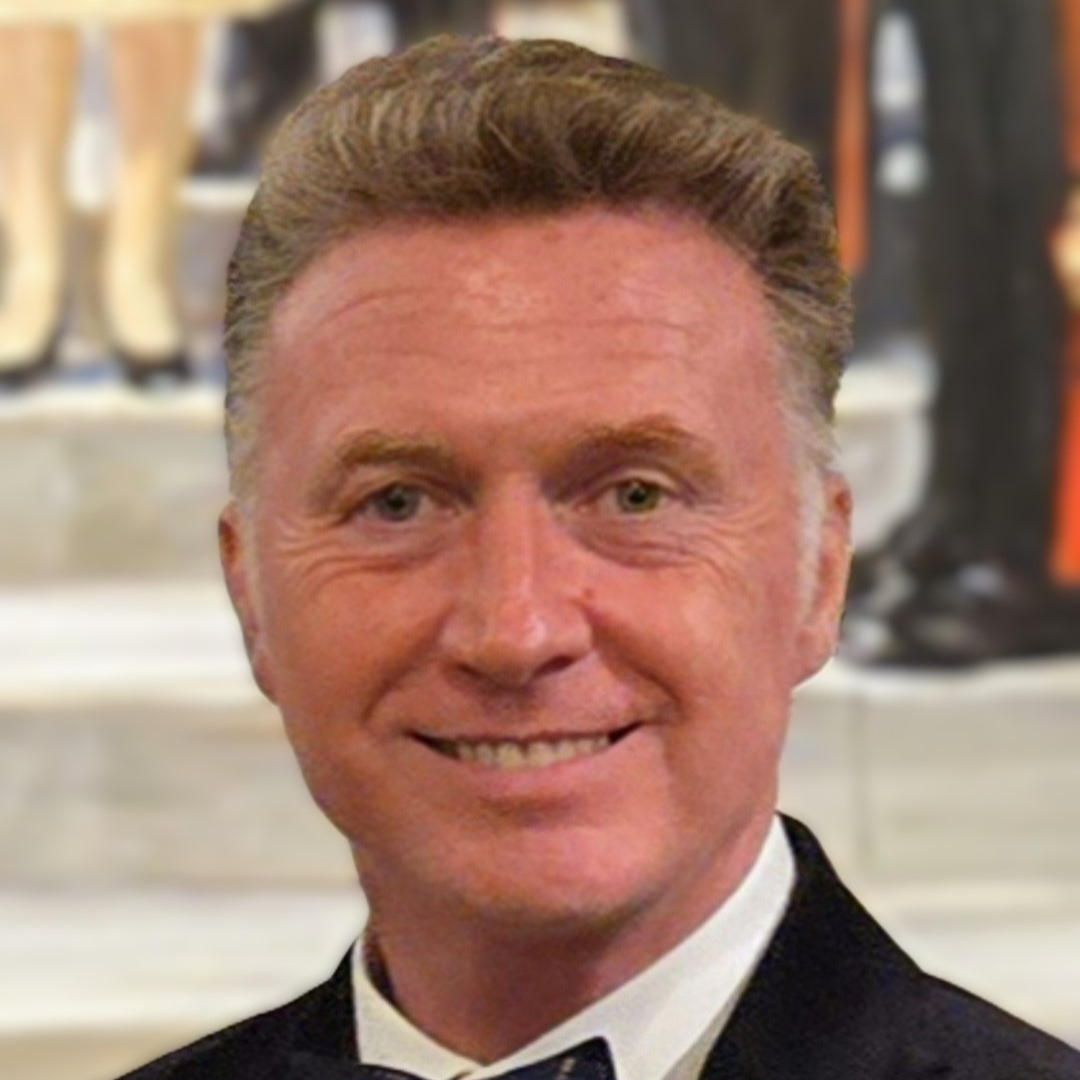 A headshot of a smiling Cllr Liam Kelly in a black suit at a formal event.