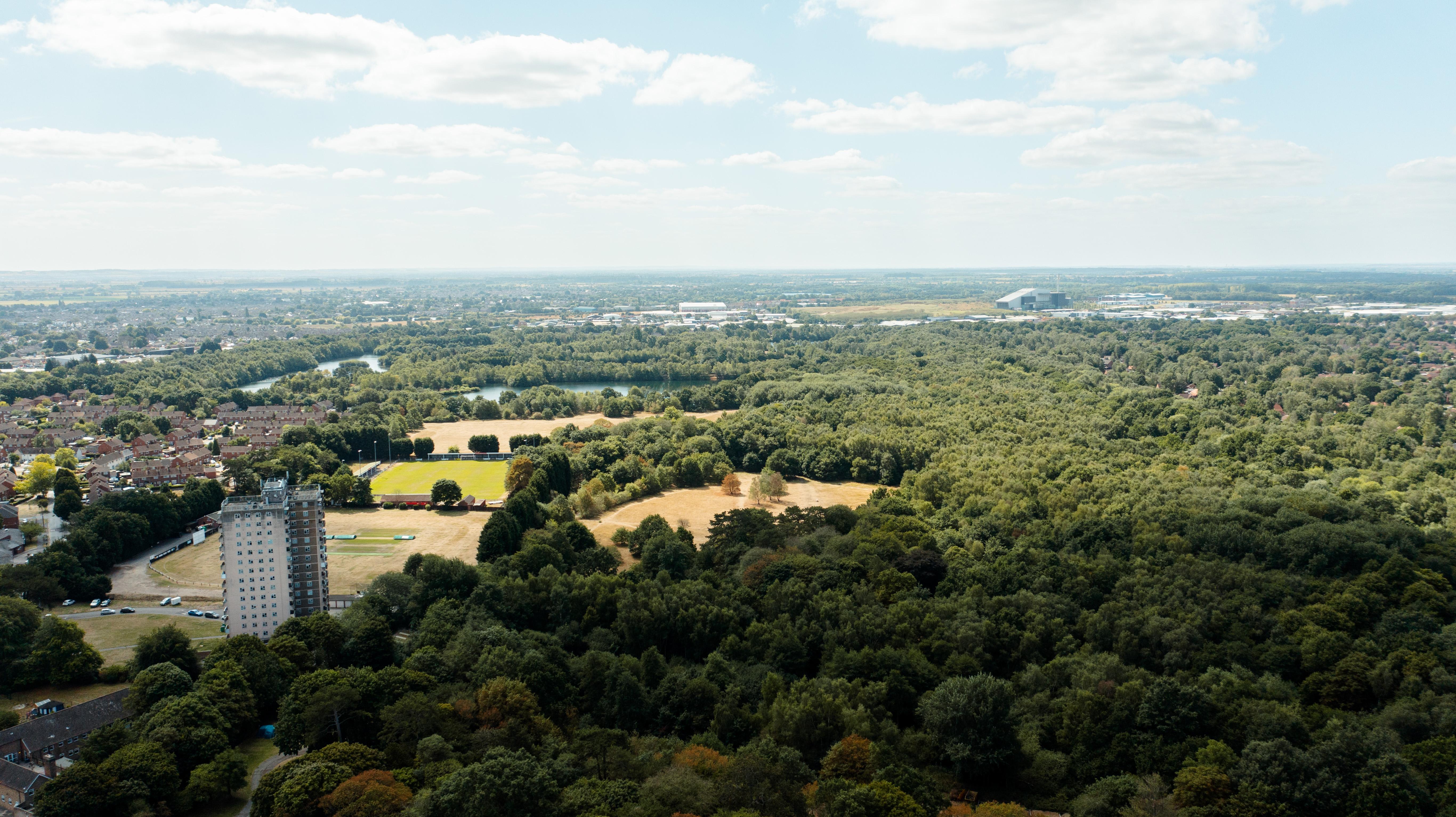 A drone view of Lincoln, with many green bushy trees and a high rise block of flats.
