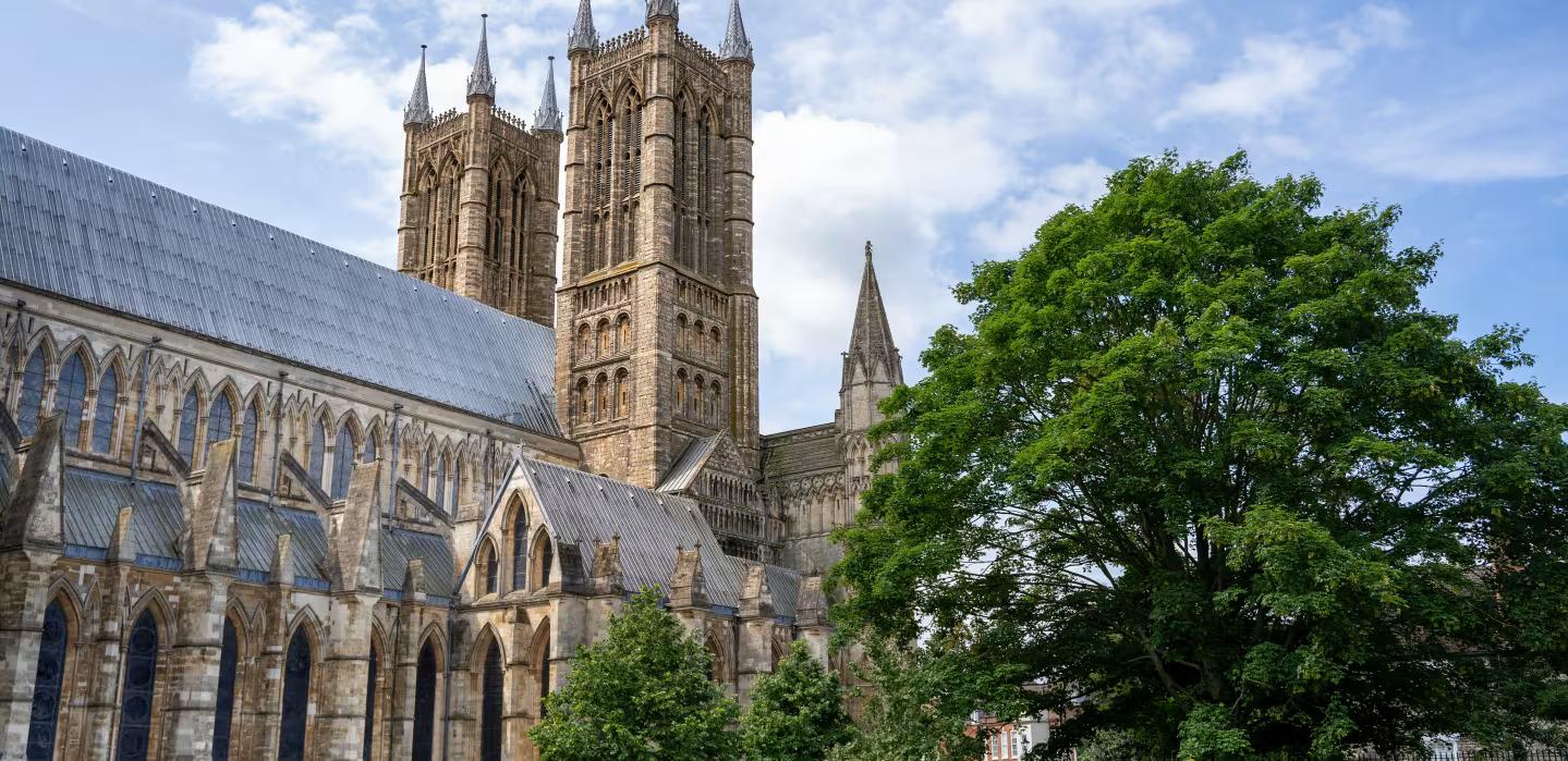 An exterior photo of Lincoln Cathedral with a green tree in front of it.