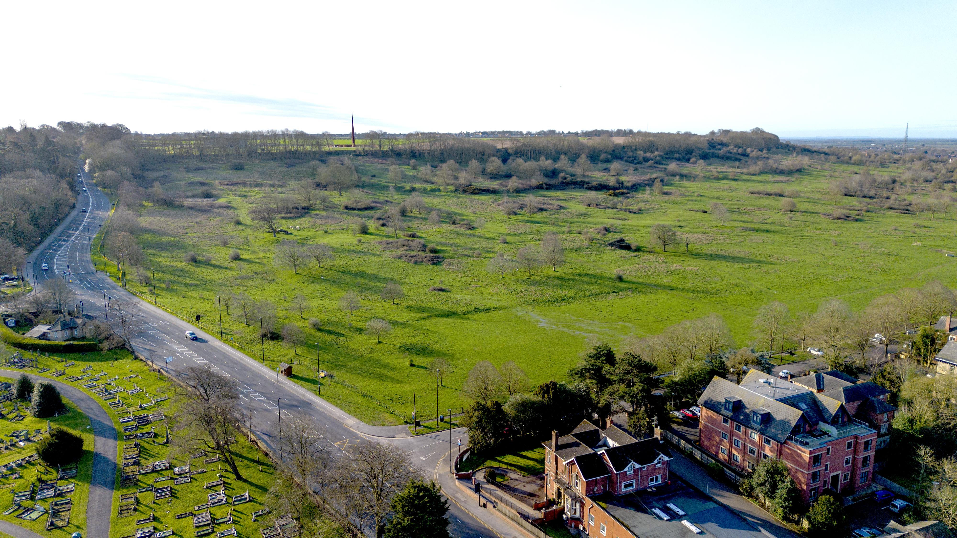 A drone image of a large grassy field next to a main road.