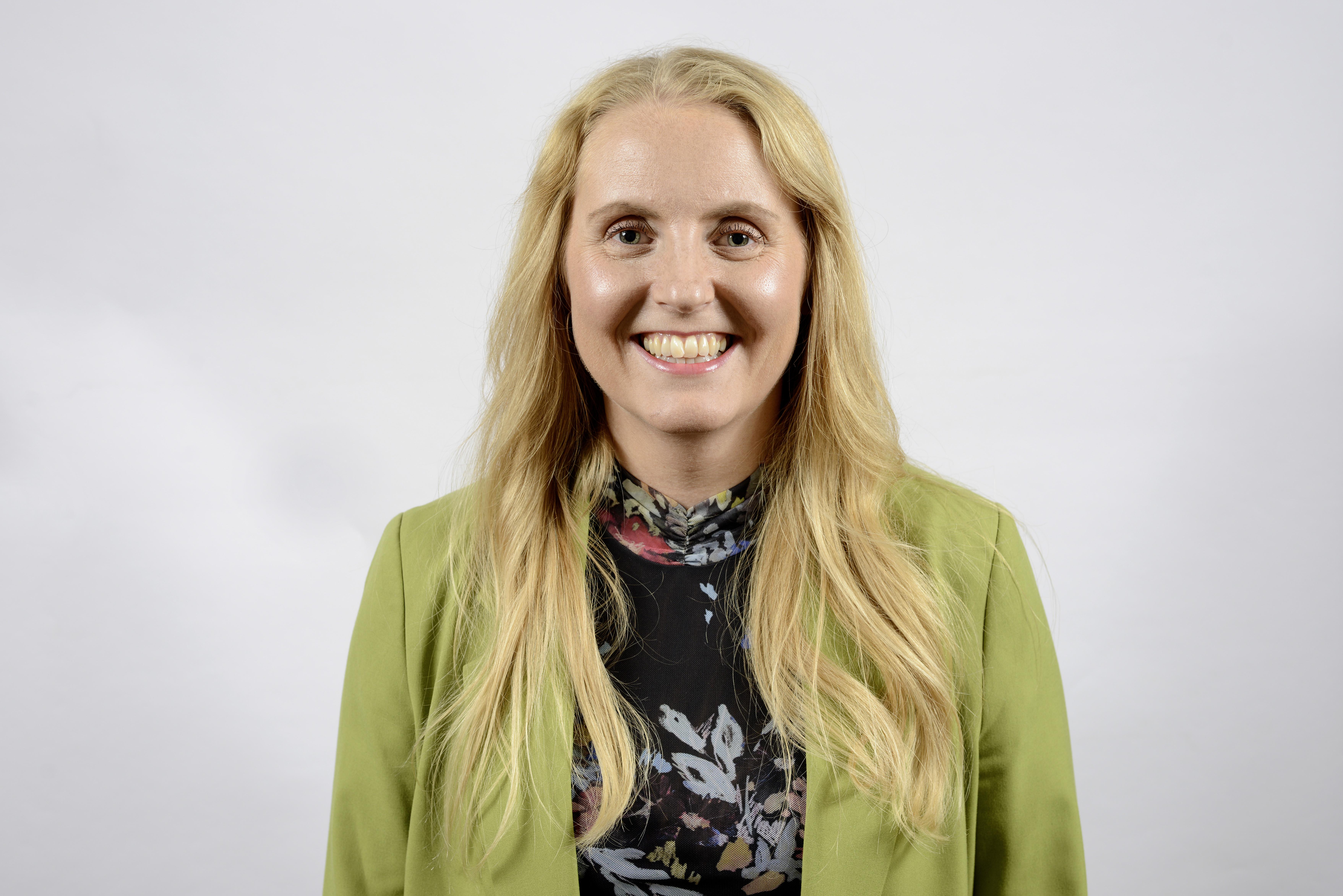 A young white woman with blonde hair smiling for a posed photo wearing a lime green jacket.