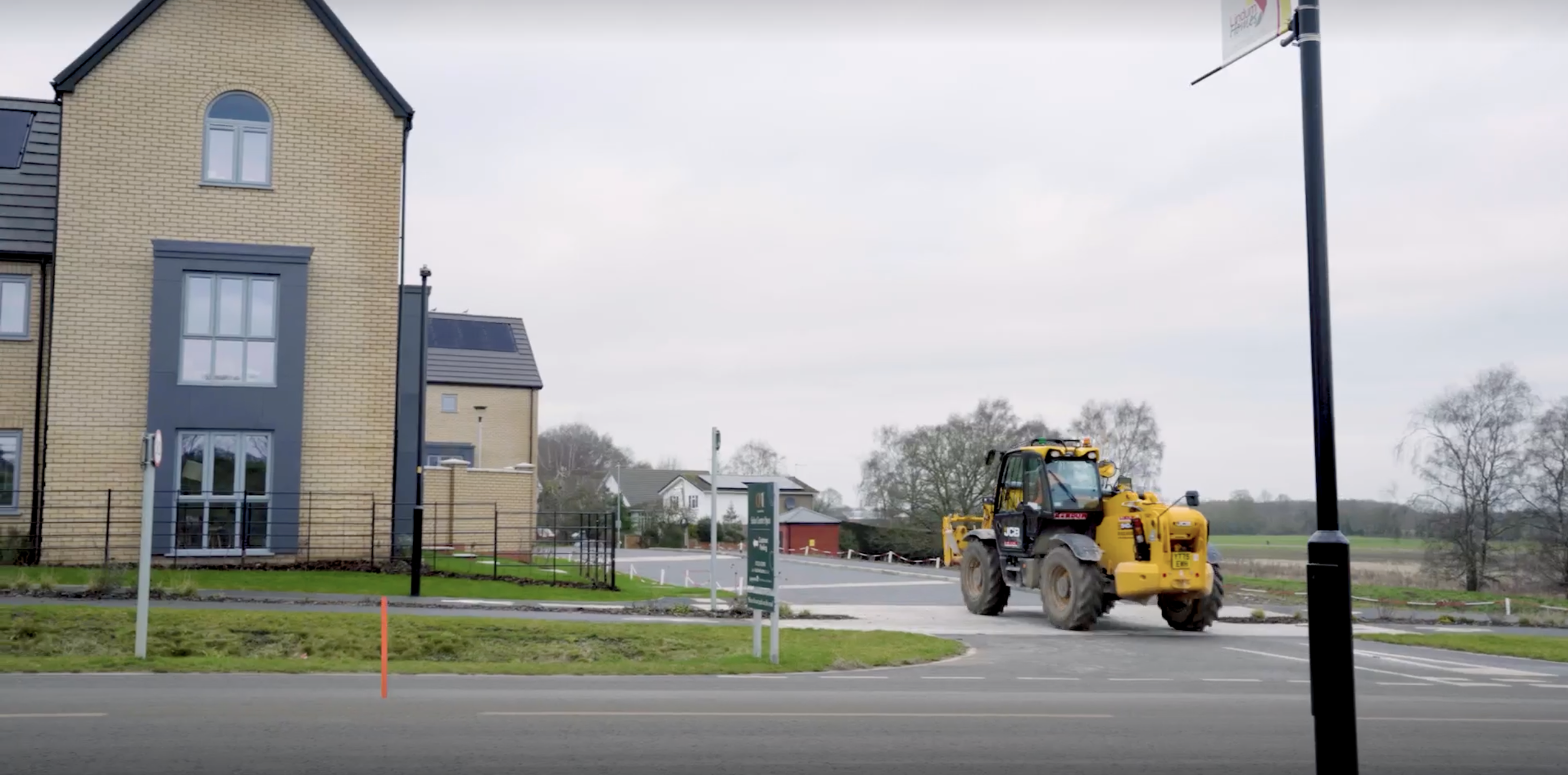 A new build house with a tractor driving on the road alongside it.