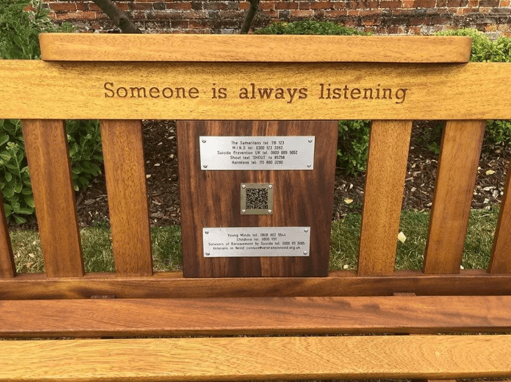 A wooden bench with contact numbers and a QR code for anyone struggling with mental health