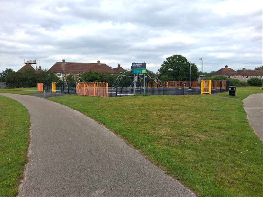 A small play park for children in a small green grassy patch between two paths that split off either side of the park.