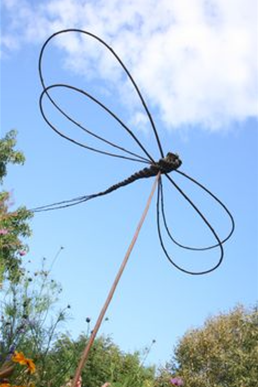A zoomed in weaved dragonfly held up in the air on a stick. There is blue sky and trees in the background.