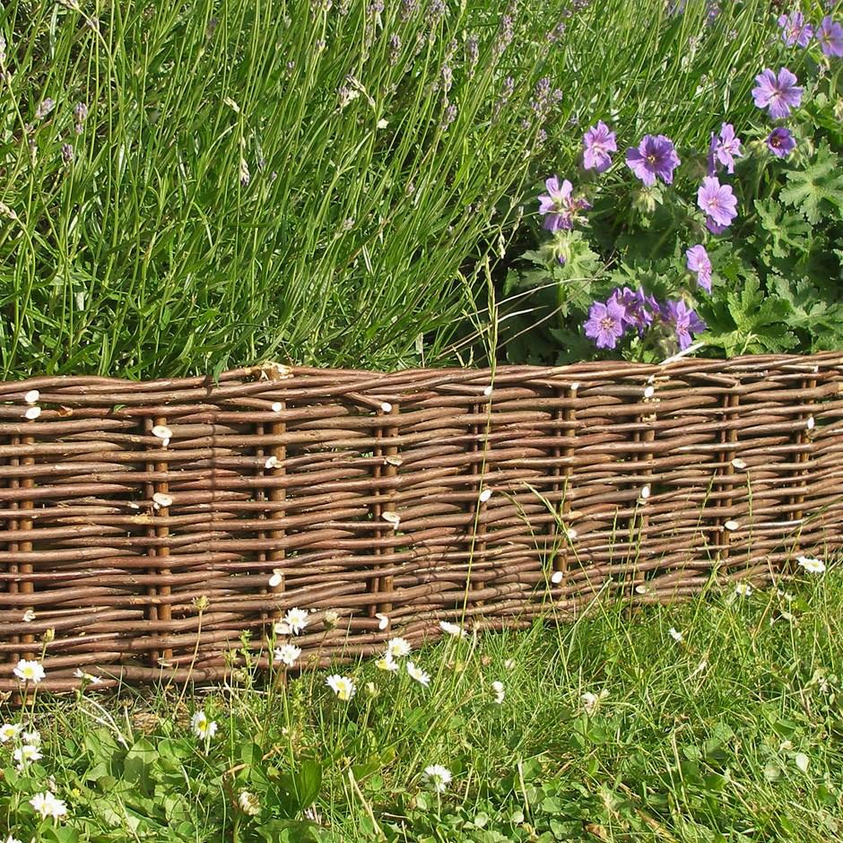 Willow edging border on the side of a garden with grass all around and purple flowers.