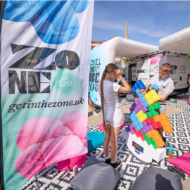 A colourful Zone Go hub on City Square, with rugs and bean bags surrounding the space. Two young people play with a giant Tetris puzzle.