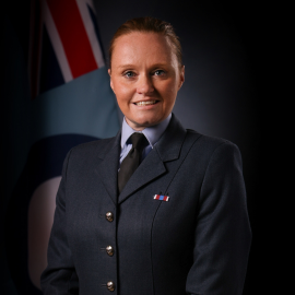 Jill stands in her Commander uniform with a British flag in the background.